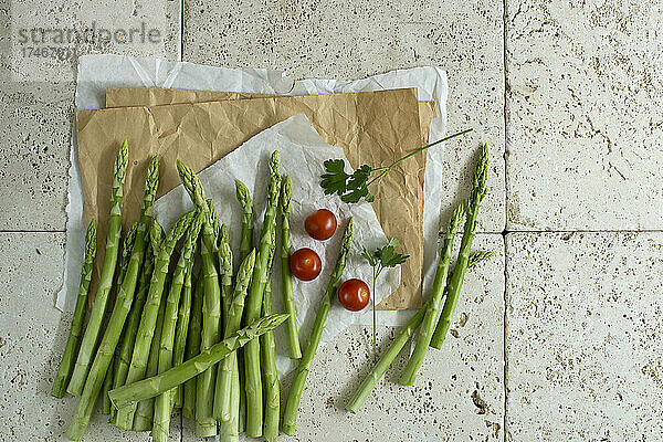Studio shot of fresh tomatoes  parsley and asparagus stalks lying on stone surface