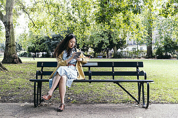 Frau liest Tagebuch  während sie auf Bank im Park sitzt