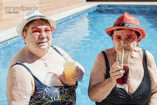 Ältere Freundinnen trinken im Sommer Saft im Schwimmbad