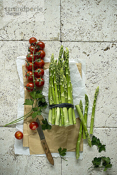 Studio shot of fresh tomatoes  parsley and asparagus bundle lying on stone surface