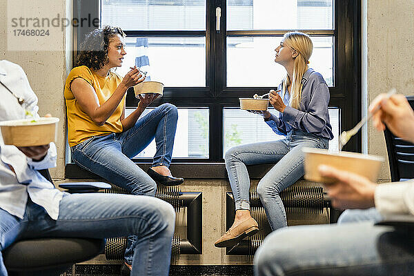Geschäftsfrauen essen mit Kollegen im Büro auf der Fensterbank