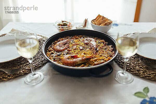 Pfanne mit verzehrfertiger Paella mit Garnelen und zwei Gläsern Weißwein
