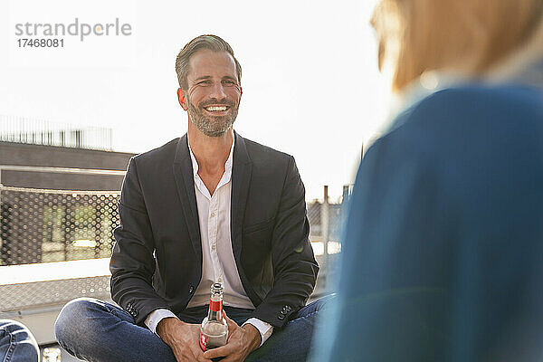 Lächelnder Geschäftsmann trinkt mit Kollegen auf der Terrasse etwas