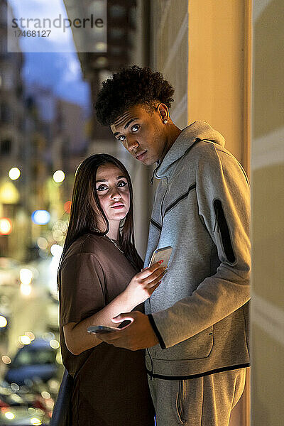 Freund hält Smartphone in der Hand  während er mit Freundin auf Balkon steht