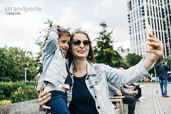 Lächelnde Mutter und Tochter machen Selfie per Smartphone im öffentlichen Park