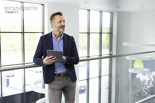 Männlicher Berufstätiger steht mit digitalem Tablet auf dem Flur im Büro