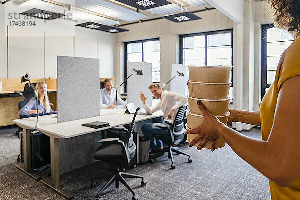 Geschäftsfrau mit Stapel Lunchboxen im Coworking Space