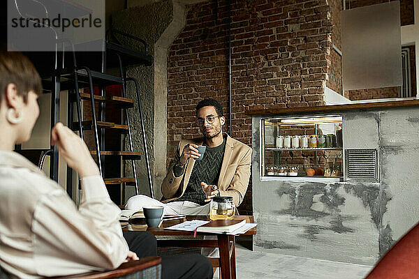 Geschäftsmann hält Tasse im Gespräch mit Kollegen im modernen Café
