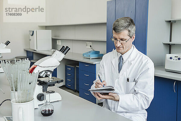 Wissenschaftler mit Brille schreibt im Labor in Notizblock