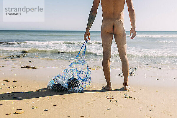 Nackter Freiwilliger sammelt Plastikmüll in einem Netzbeutel am Strand