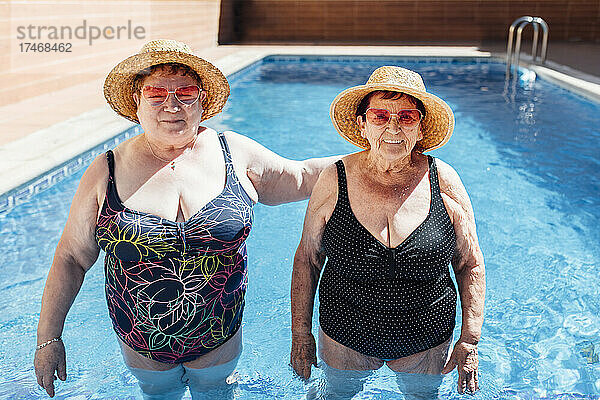 Freundinnen mit Sonnenhut stehen im Urlaub im Schwimmbad