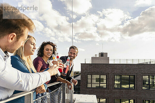 Lächelnde Kollegen stoßen auf der Terrasse mit Flaschen zu