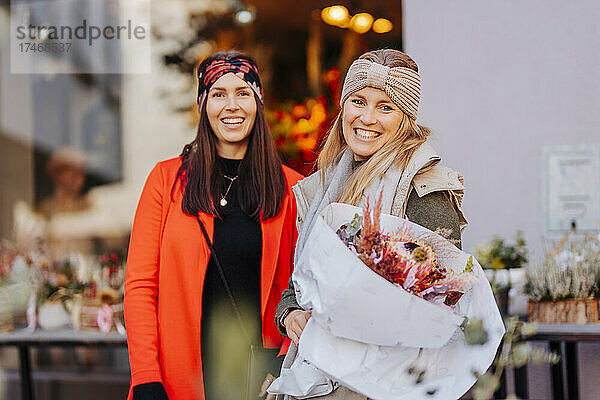 Glückliche Frau mit Blumen von einer Freundin vor dem Geschäft