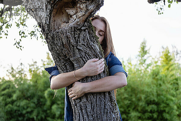 Junge Frau mit geschlossenen Augen umarmt Baum