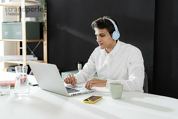 Geschäftsmann mit Kopfhörern arbeitet am Laptop am Schreibtisch im Büro