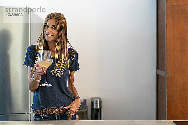 Lächelnde Frau mit braunen Haaren hält Weinglas in der Küche
