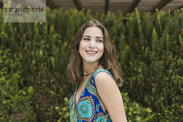 Lächelnde junge Frau vor grünem Strauch