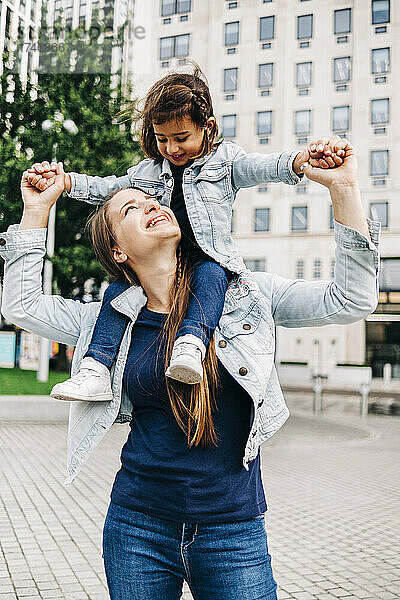 Lächelnde Mutter trägt Tochter auf Schultern im öffentlichen Park