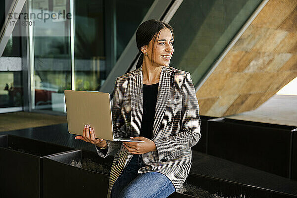 Lächelnde Geschäftsfrau mit Laptop auf der Bank