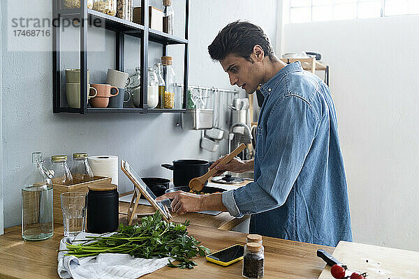 Junger Mann nutzt digitales Tablet beim Zubereiten von Speisen in der Küche