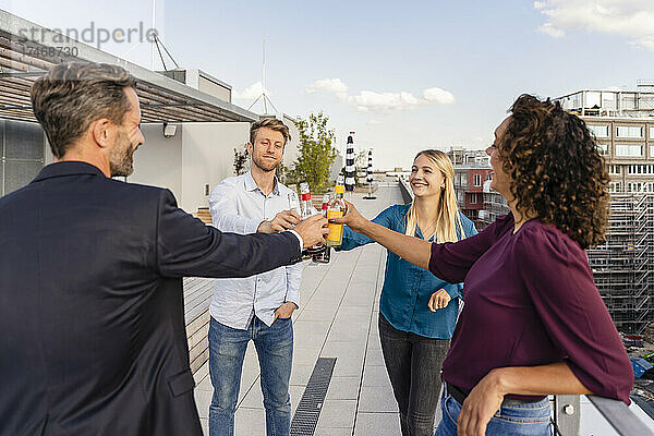 Fröhliche Kollegen stoßen auf dem Dach mit Getränkeflaschen an