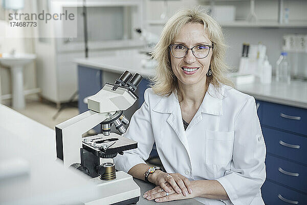 Lächelnder blonder Forscher mit Mikroskop im Labor