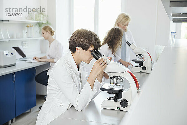 Forscher benutzen Mikroskop mit Kollegen  die im Hintergrund arbeiten