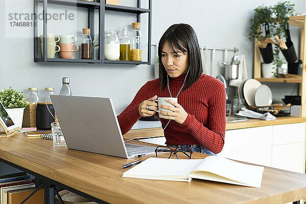 Geschäftsfrau mit Kaffeetasse arbeitet zu Hause am Laptop