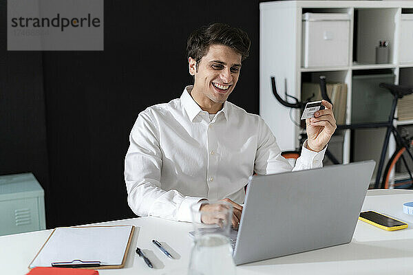 Fröhlicher Geschäftsmann beim Online-Shopping per Laptop im Büro