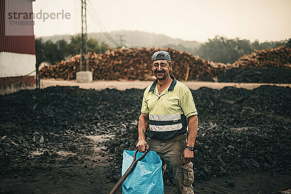 Lächelnder Arbeiter mit Plastiktüte und Werkzeug steht in der Kohlefabrik