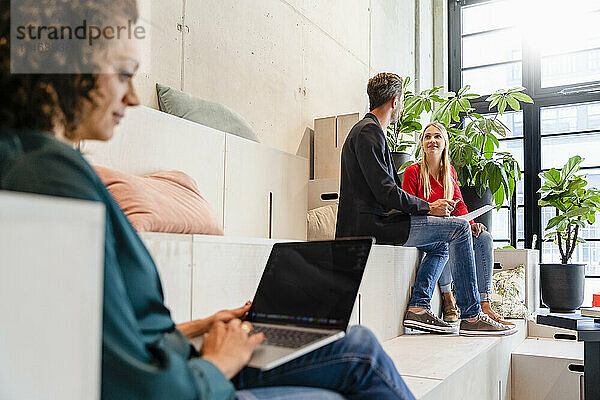 Geschäftsfrau benutzt Laptop mit Kollegen im Hintergrund im Büro