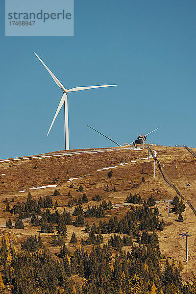 Brauner herbstlicher Bergrücken mit Windkraftanlage  die vor einem klaren blauen Himmel im Hintergrund steht