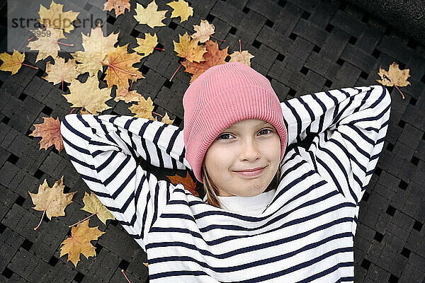 Lächelndes Mädchen mit den Händen hinter dem Kopf entspannt sich im Herbst im Park