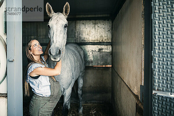 Schwangere Frau schaut Pferd im Stall an