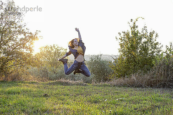 Sorglose Frau springt bei Sonnenuntergang über Gras
