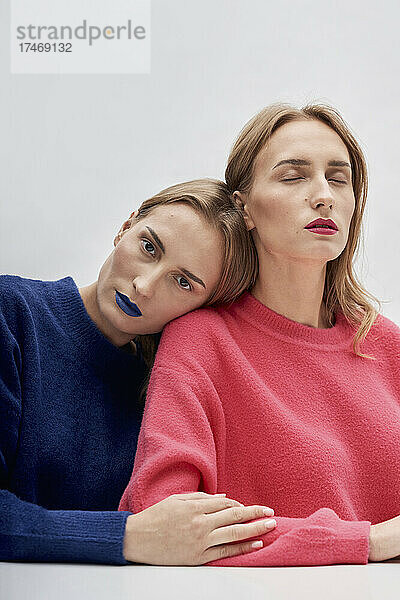 Frau mit blauem Lippenstift lehnt an der Schulter ihrer Zwillingsschwester vor weißem Hintergrund
