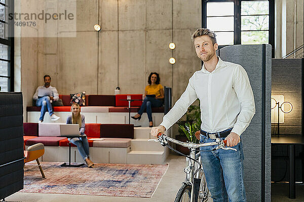 Junger Geschäftsmann mit Fahrrad im Coworking-Büro