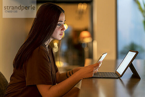 Junge Frau benutzt Smartphone und Laptop am Tisch