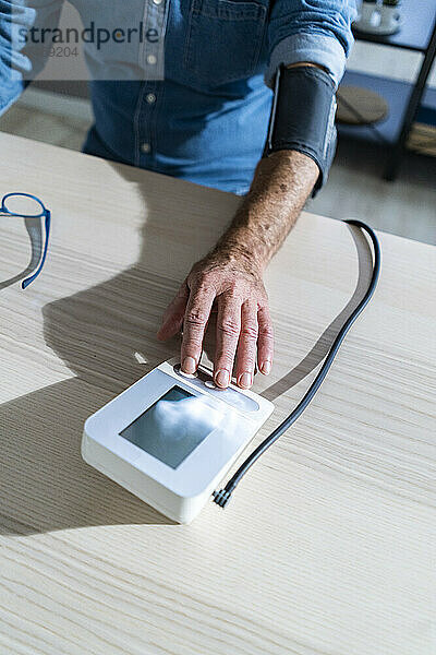 Rentner benutzt Blutdruckmessgerät am Esstisch