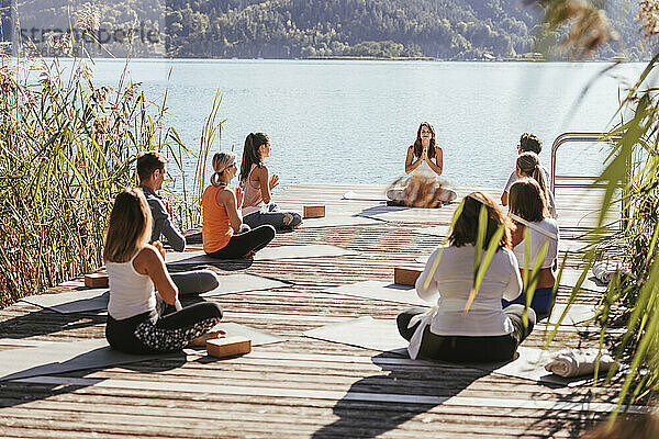 Männer und Frauen praktizieren Yoga mit einem Lehrer auf dem Steg am See
