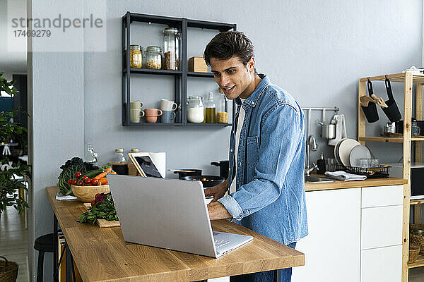 Lächelnder Mann benutzt Laptop in der heimischen Küche