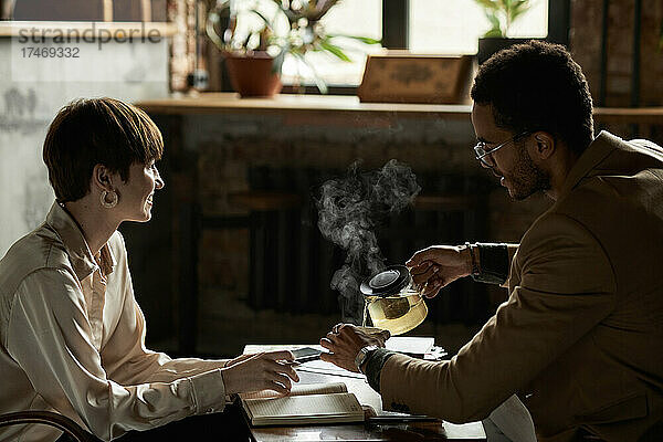 Lächelndes Teenager-Mädchen mit Mann  der im Café Tee in eine Tasse gießt
