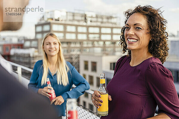 Lächelnde Geschäftsfrau trinkt mit Kollegen auf dem Dach