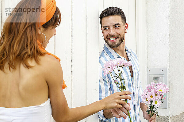 Lächelnder Mann schenkt einer Frau  die an der Wand lehnt  einen Blumenstrauß