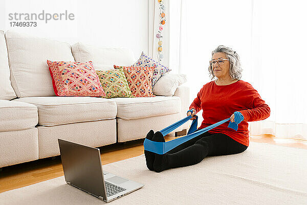 Frau macht Heimtraining  während sie sich das Tutorial auf dem Laptop ansieht