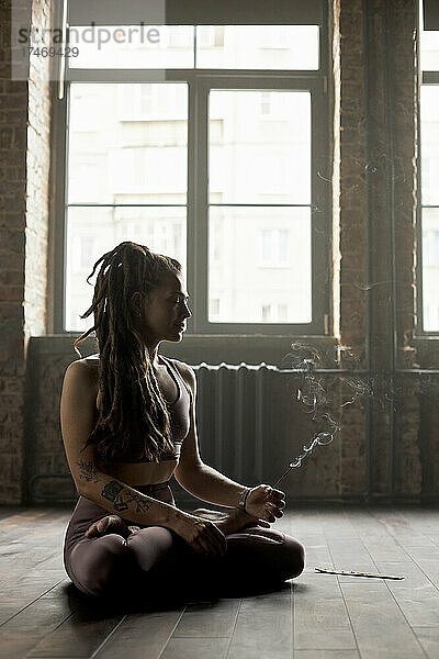 Sportlerin mit Räucherstäbchen meditiert im Yogastudio
