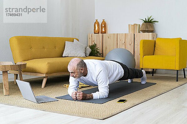 Älterer Mann mit Laptop übt Plank-Pose auf Trainingsmatte