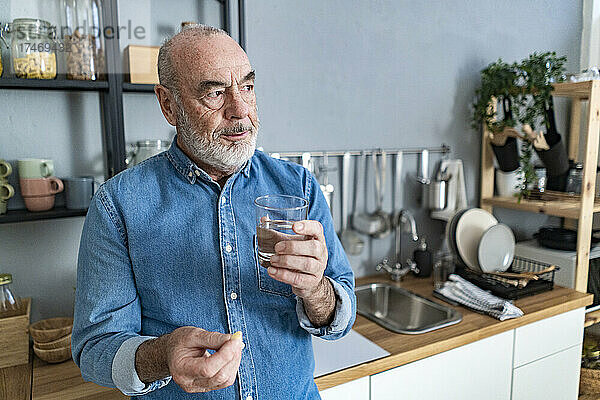 Nachdenklicher älterer Mann  der zu Hause in der Küche Medikamente einnimmt