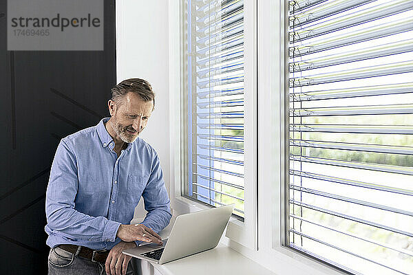 Geschäftsmann arbeitet am Laptop am Fenster im Büro