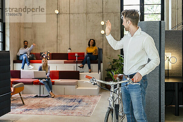 Geschäftsmann mit Fahrrad winkt Kollegen im Büro zu